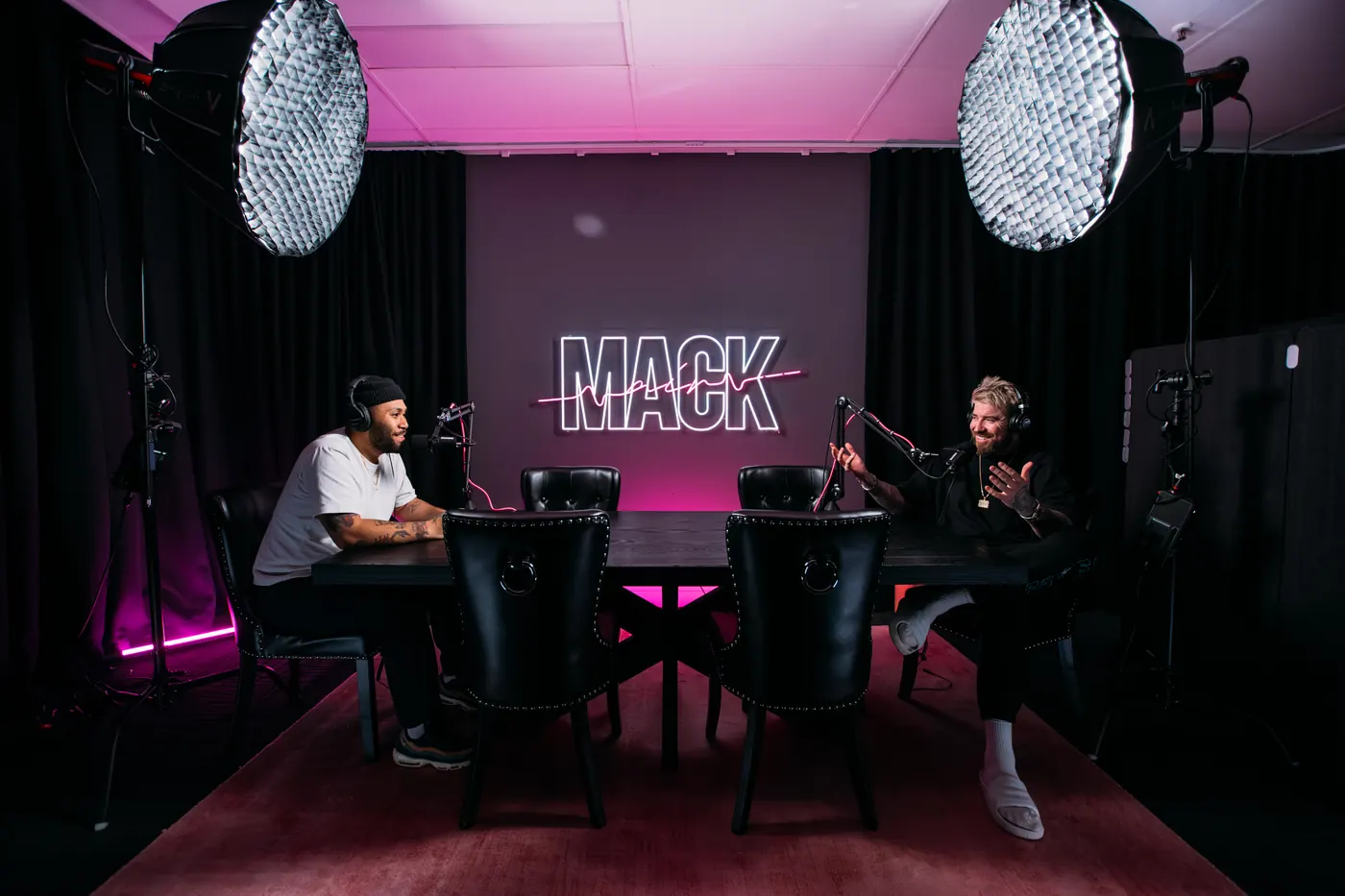 A podcast studio with two chairs under softboxes and a MACK sign in neon